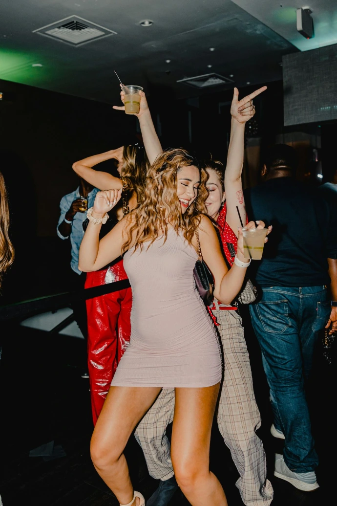 People dancing in a dimly lit club while holding plastic cups of drinks